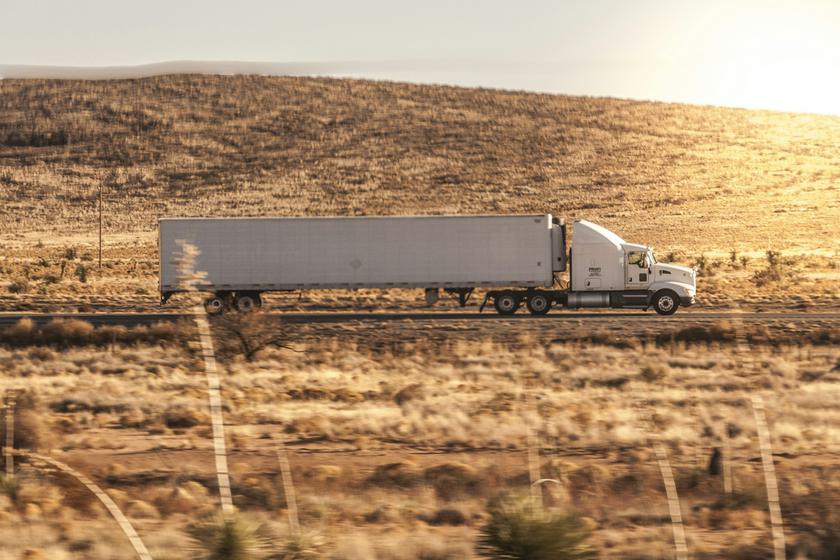 Semi truck pulling a white dry van trailer through golden hills